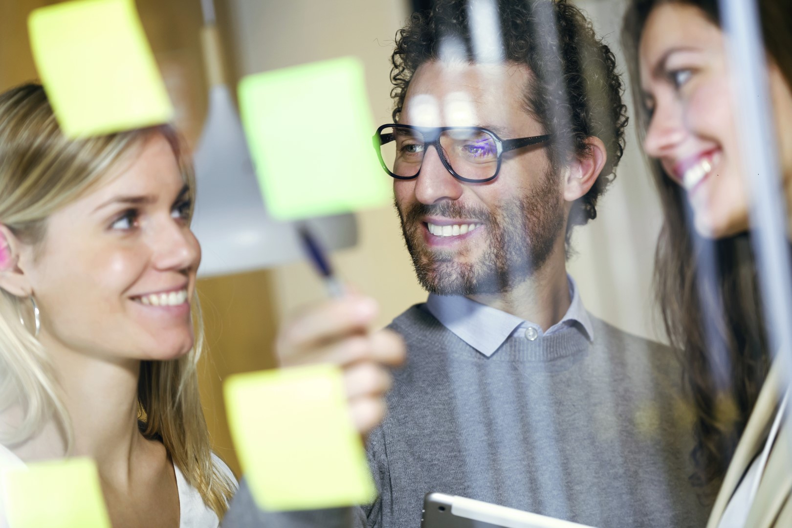 Three smiling business people brainstorming together with sticky notes on a glass wall